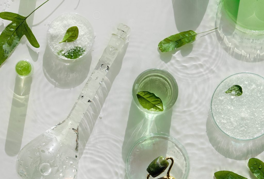 Cosmetic skincare background. Herbal medicine with green leaves. Natural sunlight, long shadows. Splashes of water, splashes. Chemical glassware, petri dishes, vials. Natural skincare background.